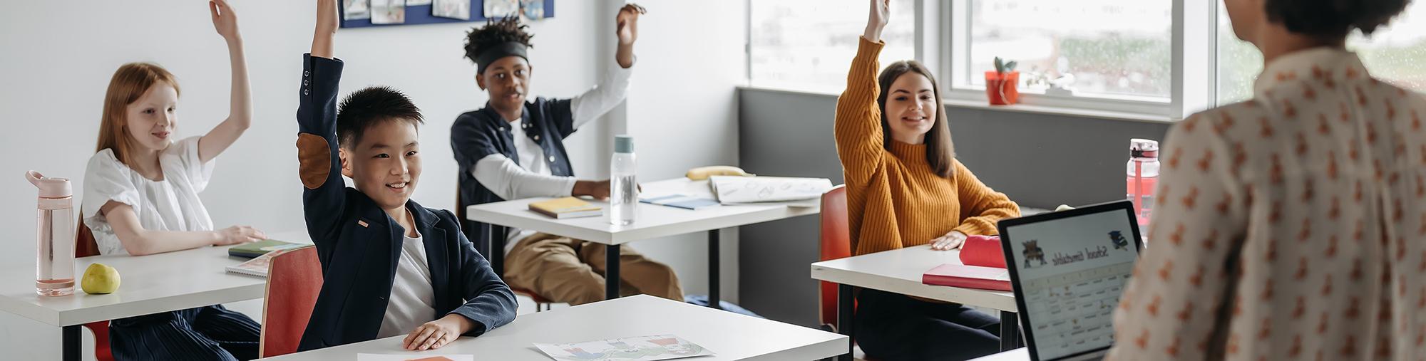 Teacher at front of classroom and students in classroom raising hands